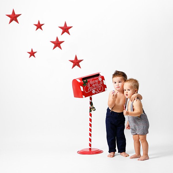 niños abrazados al lado de un buzon de papa noel y estrellas rojas