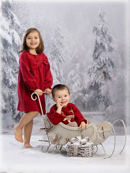 niño dentro trineo y hermana llevando trineo en paisaje de nieve navidad