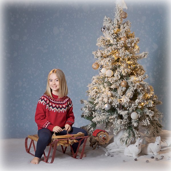 niña sentada en trineo rojo y arbol de navidad
