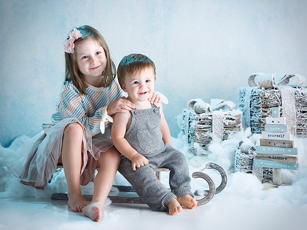 hermanos sentados en trineo, decorado nevado de navidad y regalos